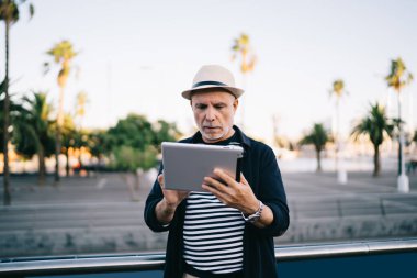 Seyahat tatillerinde modern dokunmatik kağıt kullanarak rezervasyon detaylarını kontrol etmek için 4G kablosuz internete bağlanan yaşlı erkek blogcu, Kafkas adam 60 'lı yaşlarda dijital tablet üzerinden e-posta mesajı aldı