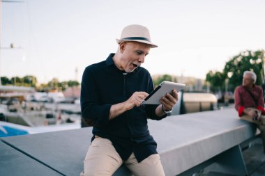 Hasır şapkalı, internetten rezervasyon yaptıran beyaz adam tek başına seyahat ederken şok olmuş, erkek turistin sosyal medyayı taramasına şaşırmış.