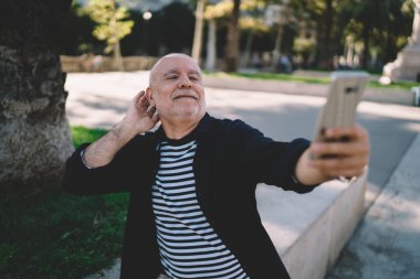 Yaşlıca erkek blogcu çekimlerinin modern cep telefonu uygulaması ile tatillerde gezinen internet kullanarak Vlog 'u etkilemesi, şehir caddesinde gündüz saatlerinde selfie akıllı telefon resimleri çekmesi