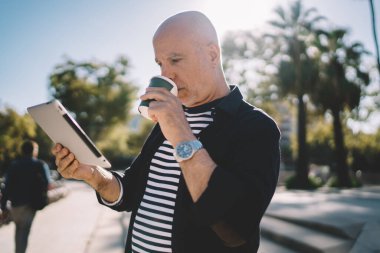 Kafkas erkek kıdemli turist kafein içeceği içerken modern dokunmatik ped aracılığıyla sosyal medyaya bağlanıyor web sitesinde seyahat tavsiyeleri okuyor, dijital tablet kullanmak için kahve ile yaşlı blogcu