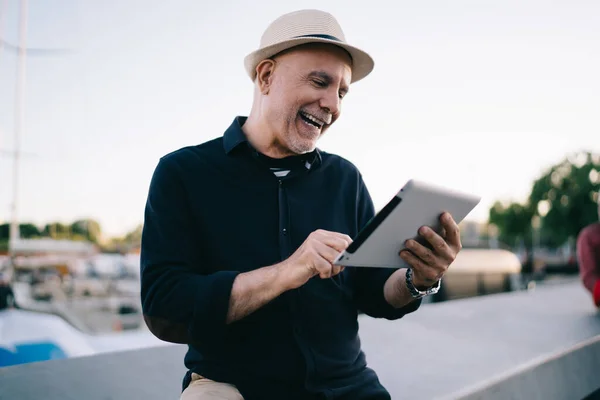 快乐的男性博主60岁 在旅行途中享受社交网络的快乐时光 享受退休生活 头戴草帽的快乐男子通过触摸板应用程序阅读有趣的出版物 — 图库照片
