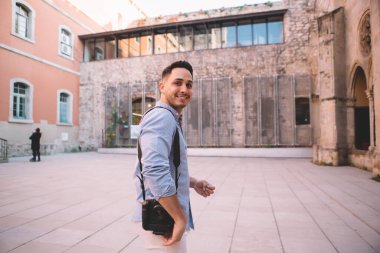 Antik kentin sokaklarında kameralı neşeli etnik adamın görüntüsü ve kameralara bakarken tatilin tadını çıkarması.