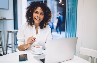 Uzaktan kumandalı kahve molasında kameraya gülümseyen, modern dizüstü bilgisayarı olan neşeli, beyaz bir kadının modern bilgisayardaki portresi.
