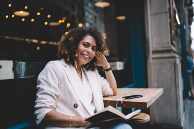 Elektronik kulaklıklı neşeli yeniyetme kızın portresi kameraya gülümserken aynı zamanda komik entrikalı pozitif sesli kitap dinliyor, tasasız milenyum kadını kaldırımda müzikle eğleniyor.