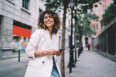 Kulaklıklı komik hippi kız haftasonu şehir yürüyüşü için pozitif müzik listesiyle boş vakitlerin tadını çıkarıyor. Duygusal kadın nesli Z, elinde cep telefonuyla sokaklarda gülümsüyor.