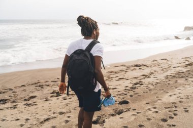 Sırt çantalı, sıradan giyinmiş, yaz mevsiminde kumsalda yürüyen isimsiz bir adamın arkadan görünüşü.
