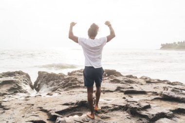 Kumlu sahilde kollarını kaldırıp özgürlüğün tadını çıkaran, sıradan giyinmiş, tanınmamış bir adam.