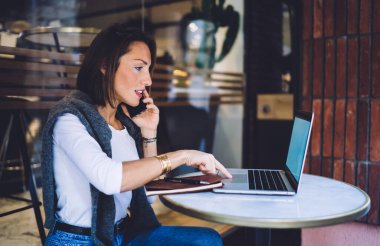 Günlük kıyafetlerle, tahta masada oturmuş laptopları karıştırırken ve kafede akıllı telefondan konuşurken yan görünüm