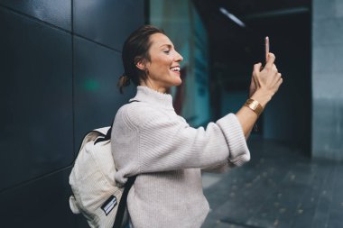 Akıllı telefon kamerasını içeriği etkilemek için kullanırken gülümseyen neşeli beyaz kadın turist, cep telefonu teknolojisiyle sosyal ağlara video bloğu çeken komik kadın