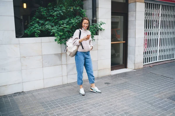 全身上下都是穿着时髦服装 背着背包的时髦女人 一边站在人行道上一边手牵着手 一边用智能手机阅读好消息 — 图库照片