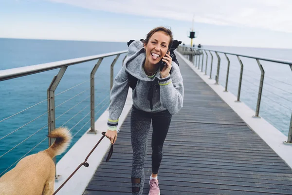 Funny Mature Female Sportswear Backpack Using Smartphone Calling Showing Tongue — Photo