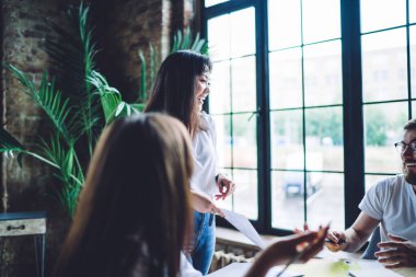 Joyful hipster guys laughing while discussing business plan during collaborative meeting for together brainstorming, group of friendly students enjoying time for analyzing course work reports