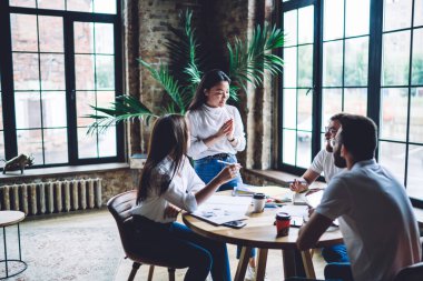 Çatı katı işbirliği sırasında okul projesini tartışan çok kültürlü öğrencilerden oluşan bir grup. Beyin fırtınası sırasında çalışan zeki erkek ve kadın analiz kağıtları.