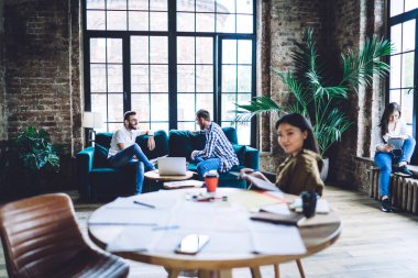 Siting diverse workers relaxing after long working day in big spacious office in loft style with modern furniture at soft daylight
