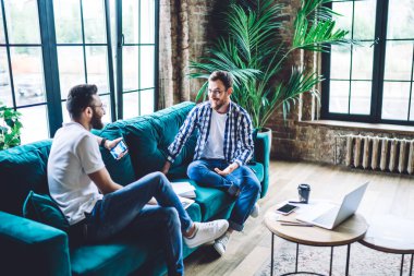 High angle of male workers in casual clothing discussing work issues while working together in stylish office with green plants