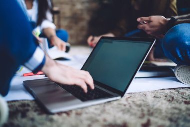 Side view of unrecognizable male in formal wear sitting on floor and browsing laptop during conversation with colleagues in office