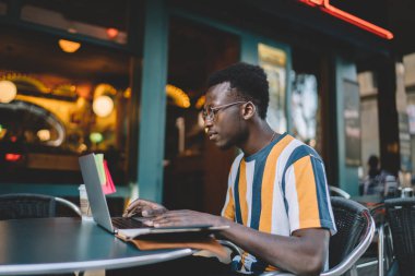 Koyu tenli yetenekli bir öğrenci. Laptop uygulaması ile öğreniyor. Sokak kafesinde otururken ve internet bağlantısı kullanırken eğitim web sitesi izliyor.