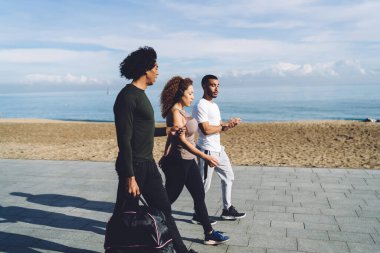 Spor çantalı çok ırklı sporcuların deniz kenarında yürürken birbirleriyle konuşmalarının yan görüntüsü.