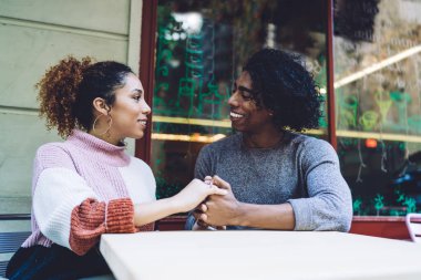 Çeşitli erkek ve kadınlar el ele tutuşup birbirlerine sevgiyle bakarken sokak kafesinde küçük bir masada oturuyorlar.