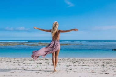 Mor elbiseli, genç ve zayıf bir bayanın kıyı şeridinde yürürken el pençe divan gezip tatilin tadını çıkardığını görüyorum.