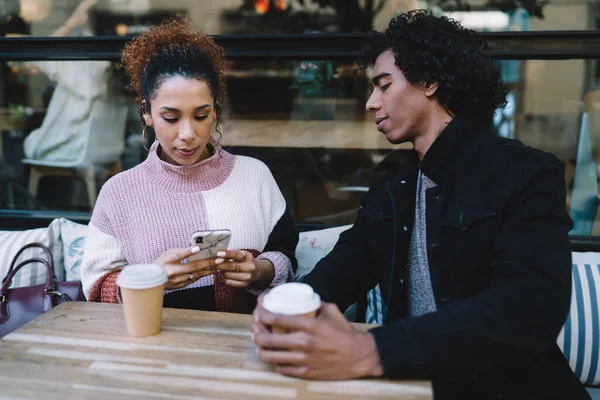 現代のカフェでコーヒーを飲みながら携帯電話を使用してカジュアルセーターで女性の友人を見て黒のジャケットで多様な若い男 — ストック写真