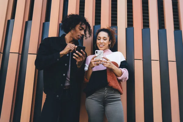 気の利いた黒人男性と笑顔の女性の下から週末に一緒に凍えている間にスマートフォンでメッセージを読んで — ストック写真