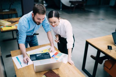 Resmi görevdeki neşeli genç iş arkadaşları masanın üzerine eğilip belgelerle ve bilgisayarla mevcut ekonomik eğilimleri analiz ediyorlar.