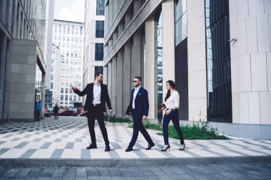 Tam vücut ciddi iş adamları resmi olarak modern binanın yakınındaki kaldırımlarda yürüyor ve gezinti sırasında iş stratejisi hakkında konuşuyorlar.