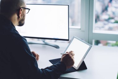 Yüksek açılı, gözlüklü, elinde boş ekranlı aletlerle masada oturan ve kripto para birimi bitcoin grafiği ile çalışan isimsiz erkek girişimcinin arka görüntüsü