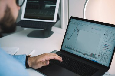 Resmi kıyafetli isimsiz sakallı bir adamın laptopuyla masada oturup bilgisayardaki kripto para birimlerini kontrol etmesi.