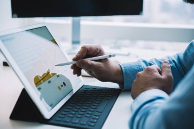 Modern iş yerinde masa başında otururken, stilus ile modern tablet kullanan isimsiz erkek işçinin yan görünüşü