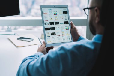Ofiste çalışırken mavi resmi gömlek ve gözlük takan, dijital tablet ve kalem kullanan sakalsız adamın arka planı.