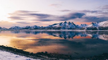 Norveç deniz suyuna yansıyan beyaz karla kaplı yüksek dağlı kayalık tepelerin nefes kesici kuş bakışı görüntüsü. Kışın Lofoten 'in nefes kesici panoramik fiyortları, doğanın sakin güzelliği. 