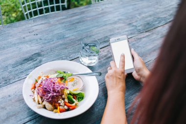 Dışarıdaki kafede sağlıklı bir öğle yemeği yerken akıllı telefondan telefonuna mesaj atan tanınmamış bir kadının arkadan görünüşü.