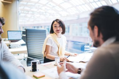 Asyalı genç bayan çalışanın proje hakkında konuşan iş arkadaşlarıyla toplantı masasında oturması üzerine seçici bir odak noktası.