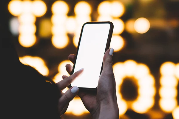 夜に輝く看板近くの通りに立っている間 現代の携帯電話を使用して手入れの行き届いた手で匿名の女性をトリミング — ストック写真