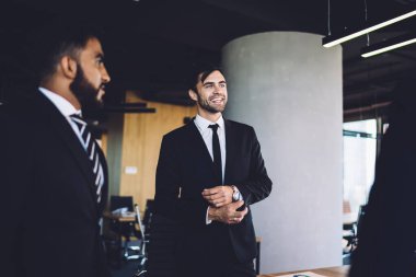 Bir grup neşeli ofis çalışanı kurumsal yenilikler hakkında konuştukları için iş toplantısından keyif alıyorlar, başarılı erkek profesyonel uzmanlar işbirliği sırasında finans ve gülümseme hakkında iletişim kuruyorlar.