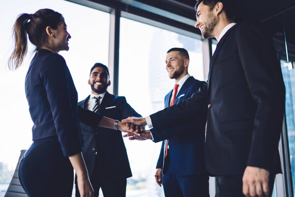 Group of happy well dressed partners stacking hands in support while looking at each other standing in front of panoramic window in conference room