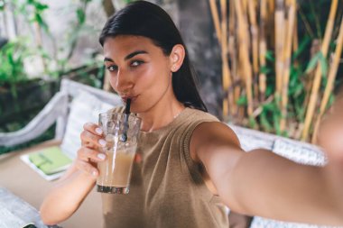 Tropikal kafede dinlenen, Bali 'de buzlu kahve içen ve selfie çeken rahat bir kadın.