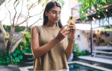 Tatil sırasında cep telefonuyla video izlerken otel bölgesinde bilardo masasında duran gözlüklü genç etnik bayan misafir.