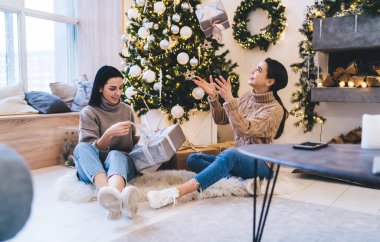 Haftasonu evde birlikte vakit geçirirken yumuşak halıda, ellerinde karton kutularla oturan mutlu kadınlar.
