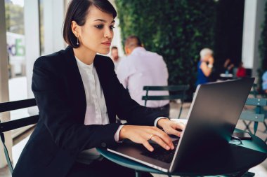 Esnek çalışma saatleri olan esmer bir kadın. Günlük rutin işlerinde tek başına otururken dizüstü bilgisayara ve klavyeye odaklanmış.