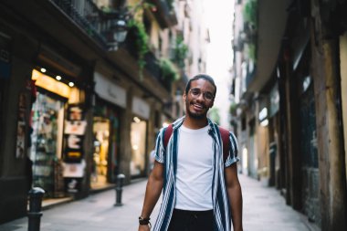 Keyifli esmer erkek gezginin yarım boy portresi. Şehir caddesinde durmuş, ziyaret yerinin keyfini çıkartıyor. Tarihi yolculukta mutlu Afrikalı Amerikalı hipster adam.