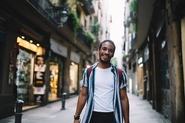 Keyifli esmer erkek gezginin yarım boy portresi. Şehir caddesinde durmuş, ziyaret yerinin keyfini çıkartıyor. Tarihi yolculukta mutlu Afrikalı Amerikalı hipster adam.