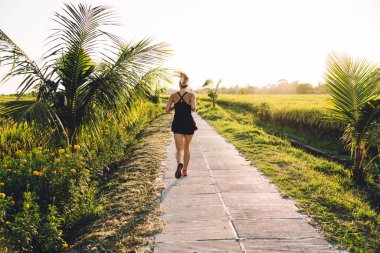 Güneşli bir günde Bali 'deki yemyeşil pirinç tarlaları arasında boş patika boyunca koşan yüzü olmayan kadın.