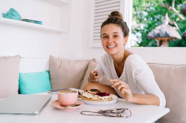 Büyük yastıklarıyla rahat koltukta oturan keyifli bir kadın ve kameraya bakarken lezzetli yiyecekler ve taze içecekler.