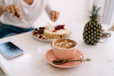 Kahvaltı masasında çay kaşığı çay kaşığı ve anananaslı pembe kahve fincanından. Bu arada anonim kadın sabah yemeği yiyor.