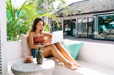 Rahat koltukta oturan ve Bali 'de dinlenirken dizüstü bilgisayarda yazan düşünceli kadın.