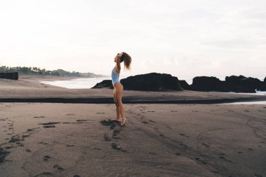 Çıplak ayaklı, seksi yüzsüz, mayo giymiş, kumlu sahilde duran ve Bali 'de yaz tatilinin tadını çıkaran bir kadın.