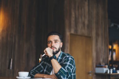Düşünceli erkek şair elinde kalemle kafeteryanın içinde boş zamanlarında yaratıcı bir fikir düşünüyor. Kafein kapuçinosu olan düşünceli hippi adam kafeterya masasında oturuyor ve kafa yoruyor.